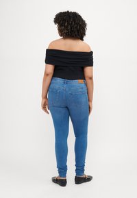 Black off-the-shoulder top and blue skinny jeans with a tan leather patch on the back waistband. Smooth texture, fitted design.