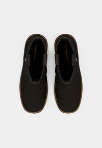 Des chaussures noires à enfiler avec une texture lisse, comportant deux lanières en tissu décoratives, des coutures contrastées et une semelle robuste.