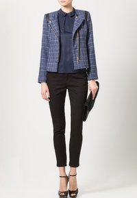 Marinblå tweedmotorcykeljacka med svarta läderdetaljer, parat med en marinblå blus och svarta figursydda byxor, kompletterat med svarta högklackade skor.