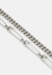 Silver metal chain featuring interlocking links, with a textured design and large safety pin accents integrated into the structure.