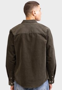 Camicia in corduroy verde scuro con colletto strutturato, maniche lunghe e polsini con bottone. Presenta righe verticali e una vestibilità morbida.