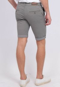 Shorts en coton gris avec des revers roulés, dotés de poches arrière et d'une étiquette sur la ceinture. Portés avec des baskets blanches.