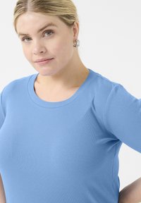 Top de manga corta acanalado en azul claro con cuello redondo. Textura suave, ligero estiramiento, diseño ajustado y una silueta cómoda.