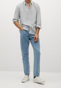 Koszula w paski, zapinana na guziki, z długim rękawem w jasnoszarym i białym kolorze, zestawiona z jasnoniebieskimi dżinsami i białymi sneakersami. Casualowy krój, wykonana z bawełny.