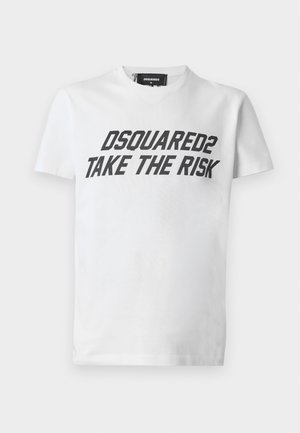 Млад мъж, облечен с бяла тениска "DSQUARED2 TAKE THE RISK", износени дънки, жълти ботуши, каре риза, завързана около кръста, и черна шапка.