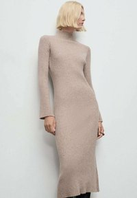 Abito in maglia a coste beige con collo alto e maniche lunghe, caratterizzato da una silhouette aderente e una leggera svasatura all'orlo.