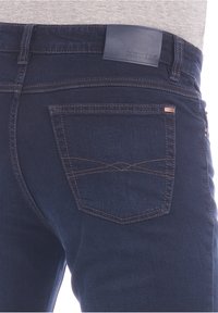 Jeans de mezclilla azul oscuro con una etiqueta de cuero en la cintura. Presenta un bolsillo trasero con costuras decorativas en un patrón de diamante.