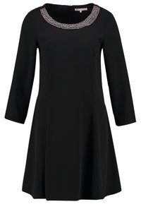 Robe noire trapèze à manches longues, dotée d'un col rond orné de perles et d'une texture lisse. Fermeture zippée au centre du dos.