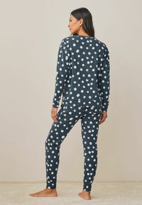 Marinblå pyjamasset med prickar, bestående av en långärmad topp och byxor med elastisk midja, tillverkad av mjukt material och med vita cirkulära mönster.