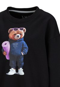 Zwarte sweatshirt met een berenprint in een blauwe hoodie, witte sneakers en paarse zonnebril, die een roze yogamat vasthoudt.