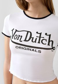 Weißes, kurzes T-Shirt mit schwarzem Saum, das ein auffälliges schwarzes Logo "Von Dutch Originals" in verblasster Schrift und einem gewellten Saum zeigt.