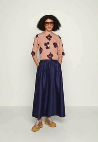 Blusa rosa de mangas curtas com estampa floral e pétalas escuras, combinada com uma saia longa azul-marinho. Modelo a usar sapatos de salto grossos em tom de bege.