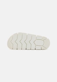 White shoe sole with deep grooves and a zigzag pattern, featuring raised sections for traction and a rounded toe. Durable rubber material.