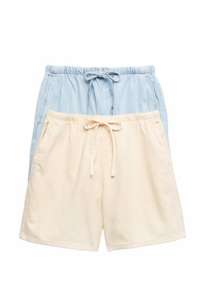Kvinde iført en blå smock-top, lyse denimshorts, brune snørestøvler og en denimjakke hængende over skuldrene.