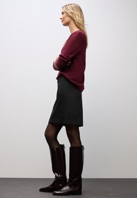 Pull en tricot bordeaux, jupe noire à mi-mollet, collants noirs transparents et bottes marron brillantes jusqu'au genou avec un zip sur le côté.