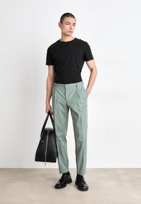 T-shirt noir à manches courtes, pantalon vert menthe, chaussures en cuir noires et tenant un sac noir avec une fermeture éclair argentée. Design simple et moderne.