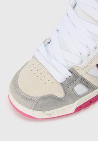 Sneaker featuring a gray suede and cream upper, white laces, and a pink rubber sole. Perforated details near the toe for breathability.
