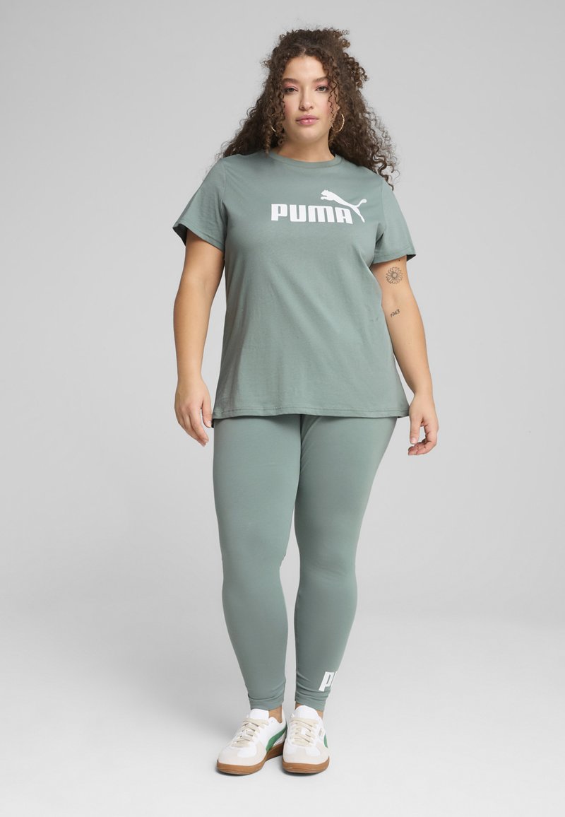 Světle zelené bavlněné tričko s logem "PUMA", spárované s odpovídajícími legínami. Boty jsou bílé s zelenými a hnědými akcenty.