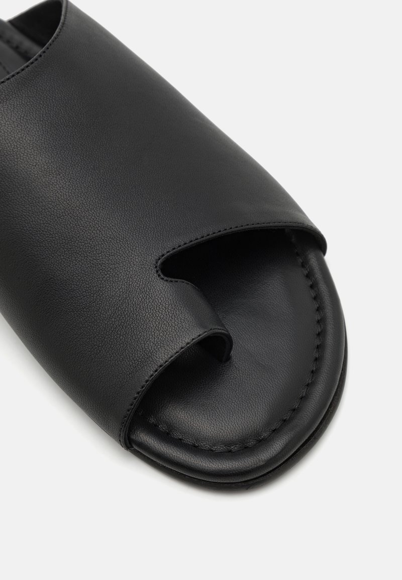 Sorte læderslippers med åben tå-design, glat tekstur og diskrete stikninger langs kanterne. Rund sål.