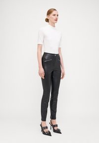 Svarta fusk läderbyxor med dragkedjeaccenter, hög midja och slim fit, tillsammans med en vit kortärmad polotröja och svarta högklackade skor.