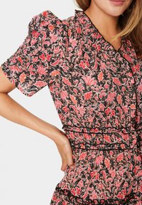 Květinové šaty s krátkými nafouknutými rukávy, s černým podkladem, růžovým a červeným květinovým vzorem a volánkovými detaily na výstřihu a pase.