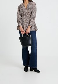 Blouse à motifs marron et blanc avec un design péplum, associée à un jean évasé bleu foncé et un petit sac à main noir. Bottines à talons noires.