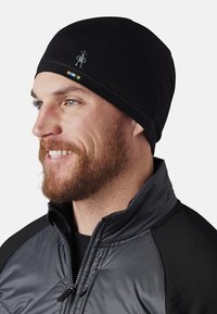 Gorra de lana negra hecha de un tejido suave, con un pequeño logotipo y rayas de acento coloridas. Se ajusta cómodamente a la cabeza.