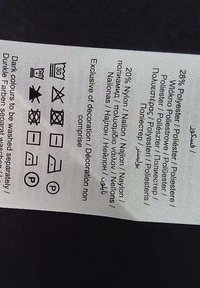 Étiquette d'entretien avec instructions de lavage et composition du matériau : 28 % polyester, 20 % nylon ; comprend des symboles de lavage et un texte en plusieurs langues.