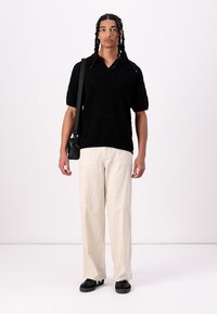 Polo shirt tricotat negru cu mâneci scurte, asortat cu pantaloni bej largi și pantofi negri, completat cu o geantă mică de umăr neagră.