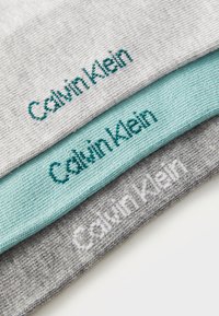 Tre par med sokker i lysegrå, middels grå og turkis farge. Hver sokk har "Calvin Klein" i kontrasterende broderi.