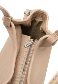 Beżowa skórzana torebka o teksturowanym wykończeniu, z zamknięciem na zamek błyskawiczny, podszewką wewnętrzną oraz srebrnym detalem na uchwycie zamka.