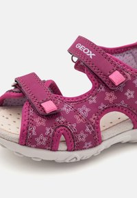 Sandalia rosa con patrón floral, dos correas ajustables, plantilla acolchada y material transpirable. Cuenta con una suela blanca texturizada para mayor agarre.