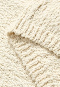 Gros plan d’un tissu tricoté couleur crème avec des motifs côtelés et torsadés montrant des plis doux et texturés du fil.