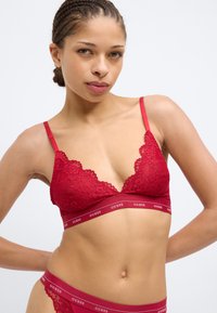 Rotes Spitzen-Bralette mit Dreieckscups, verstellbaren Trägern und einem elastischen, gebrandeten Bund. Strukturierte Blumenmuster und glatte Kanten sind sichtbar.