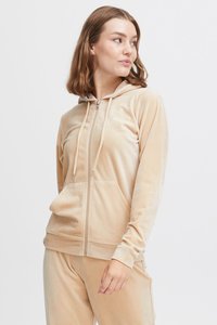 Béžová zipeová mikina z mäkkého velvet materiálu; obsahuje kapucňu, predné vrecká a šnúrky; rebrované manžety, hladký povrch a čisté línie.