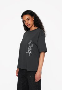 Grå bomulds T-shirt med korte ærmer, afslappet pasform, med et hvidt grafisk design på venstre side. Blød tekstur og minimalistisk stil.