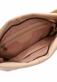 Interno della borsa beige con tasca con zip, texture liscia e fodera morbida. Presenta un'apertura arrotondata e dettagli della cerniera nera.