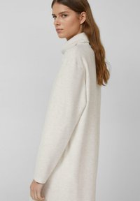 Kremowa sukienka swetrowa z wysokim kołnierzem, długimi rękawami i luźnym krojem. Gładka faktura i minimalna ilość szwów.