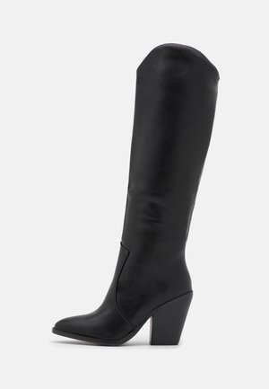Botte en cuir noire haute jusqu'au genou avec bout pointu et talon bloc empilé, vue de l'intérieur sur fond blanc.