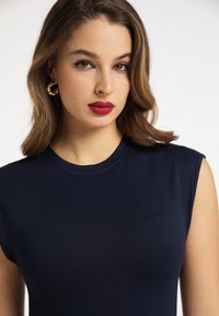 Marineblauw mouwloos topje van gladde stof met een ronde hals en minimale details. Heeft een subtiele borstzak.