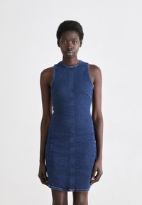 Denim brezrokavnik v temno modri barvi, slim fit, z zaobljenim izrezom, vidnim šivom in stranskimi šivi. Gladka tekstura in telo objemajoča oblika.