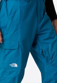 Heldere blauwe waterproof broeken van duurzaam materiaal. Kenmerken zijn onder andere een ritszijde, zakken en een wit logo op het been.