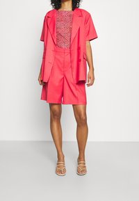 Fuchsiový dvoudílný outfit složený z volné blejzrové bundy a střižených šortek. Hlavní část má barevný abstraktní vzor, zatímco blejzr je jednobarevný.