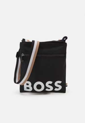 Černá crossbody taška s velkým bílým textem "BOSS", přední kapsou na zip a nastavitelným popruhem se béžovými, bílými a černými pruhy.