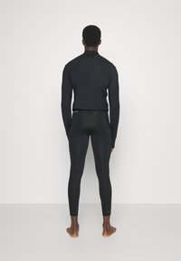 Czarny sportowy top z wysokim kołnierzem i długimi rękawami, w połączeniu z dopasowanymi czarnymi legginsami. Gładka faktura, minimalny design i brak widocznych wzorów.