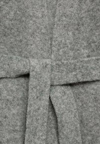 Tissu tricoté gris mettant en valeur une surface douce et texturée. Présente une ceinture à la taille, avec une teinte légèrement plus foncée pour le contraste.