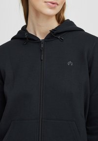 Black zip-up hoodie made from soft, textured fabric. Features a drawstring hood and a small logo detail on the chest.