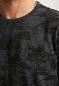 Černé tričko s jemným vzorem tmavě šedé krajiny. Má kulatý výstřih a diskrétní výšivku loga na hrudi. Hladká textura.