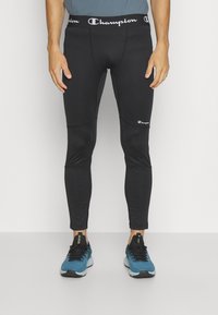 Czarne legginsy sportowe o dopasowanym kroju, z białym logo "Champion" wzdłuż pasa i gładką, jedwabistą fakturą.