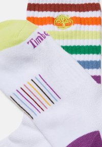 Färgglada randiga strumpor med vit bas och ränder i brunt, orange, grönt och lila, med textillogo och kontrasterande tådesign.